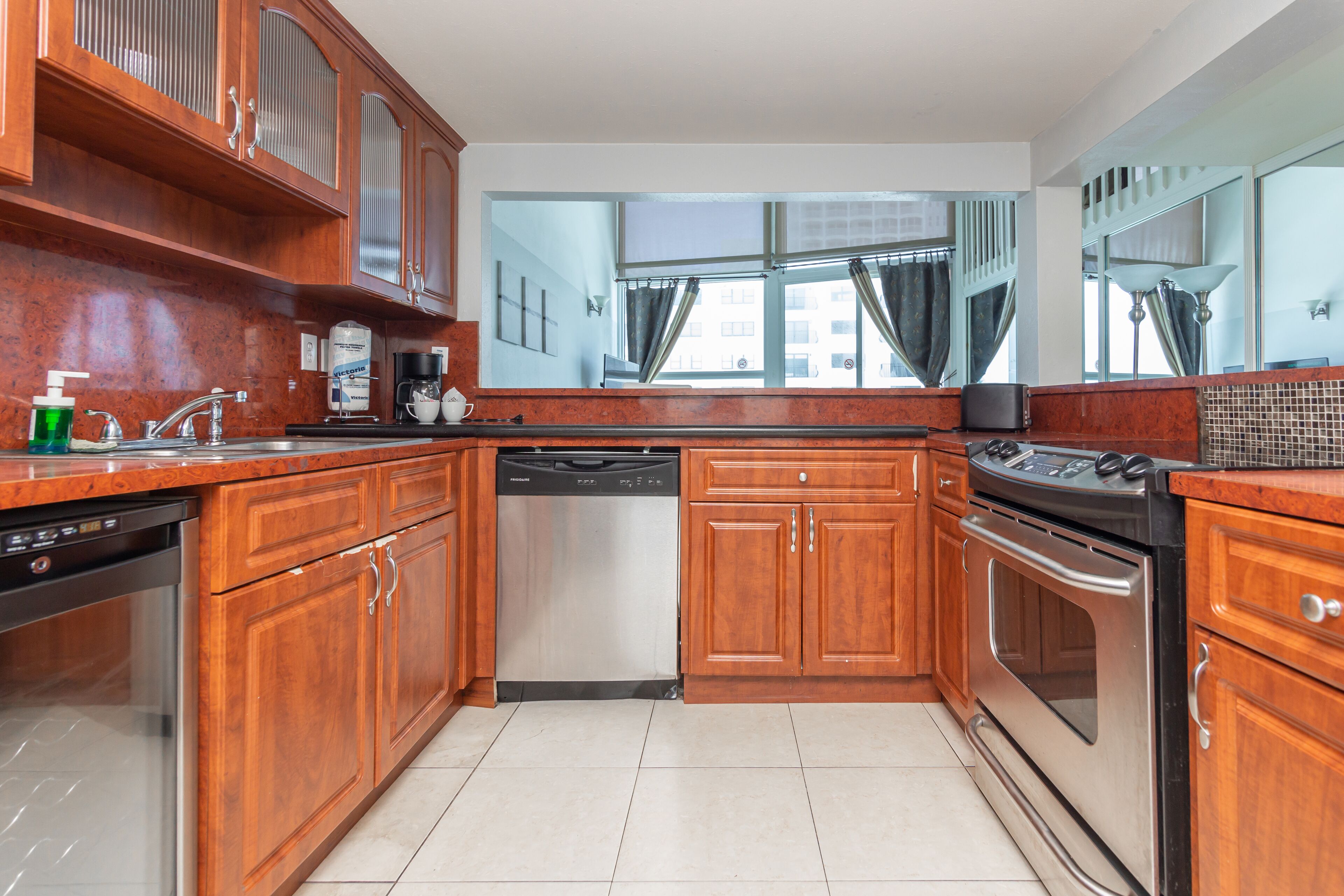 A kitchen with wooden cabinets, stainless steel appliances, and a window with curtains.