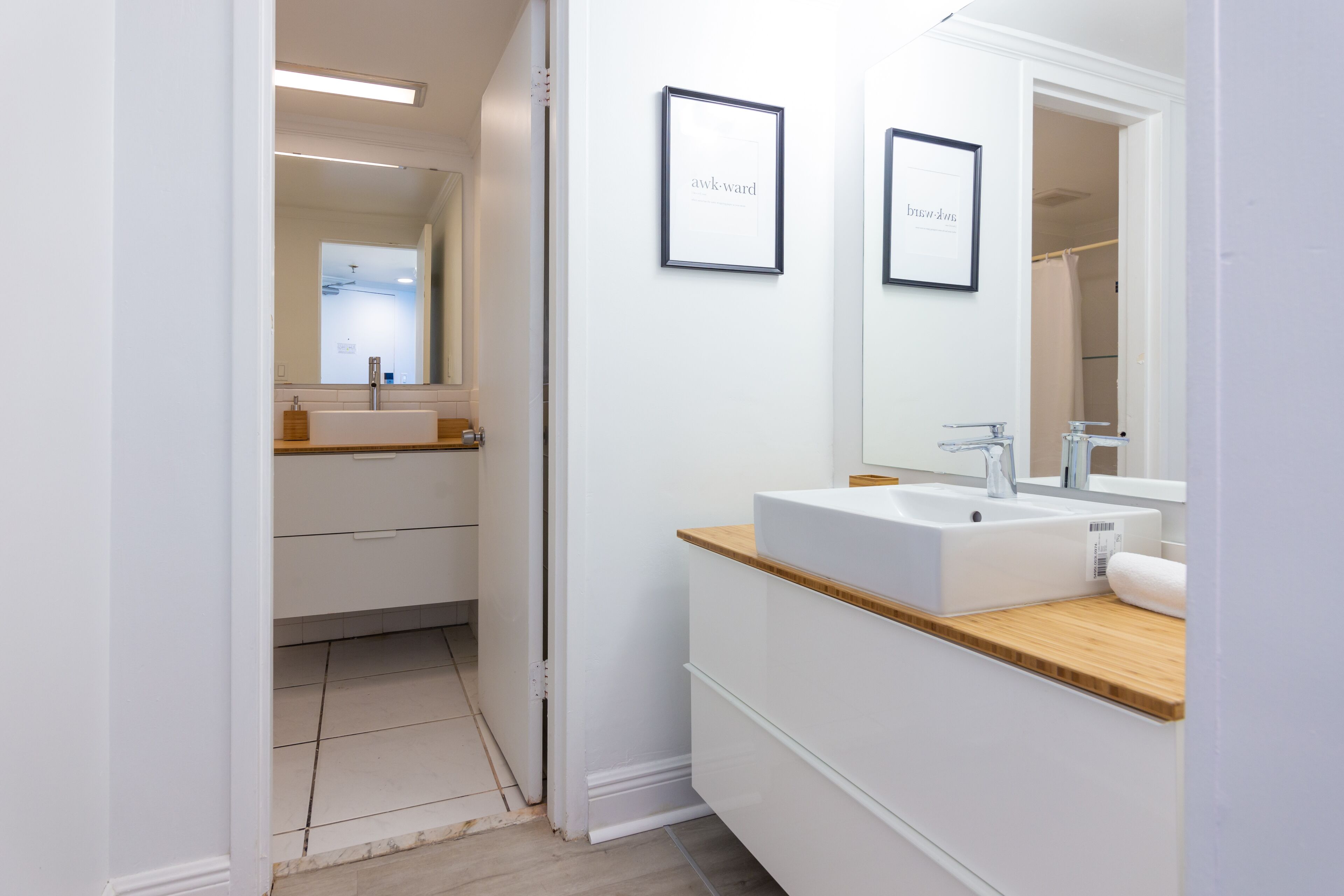 A modern bathroom with a white sink, wooden countertop, and two framed pictures on the wall.