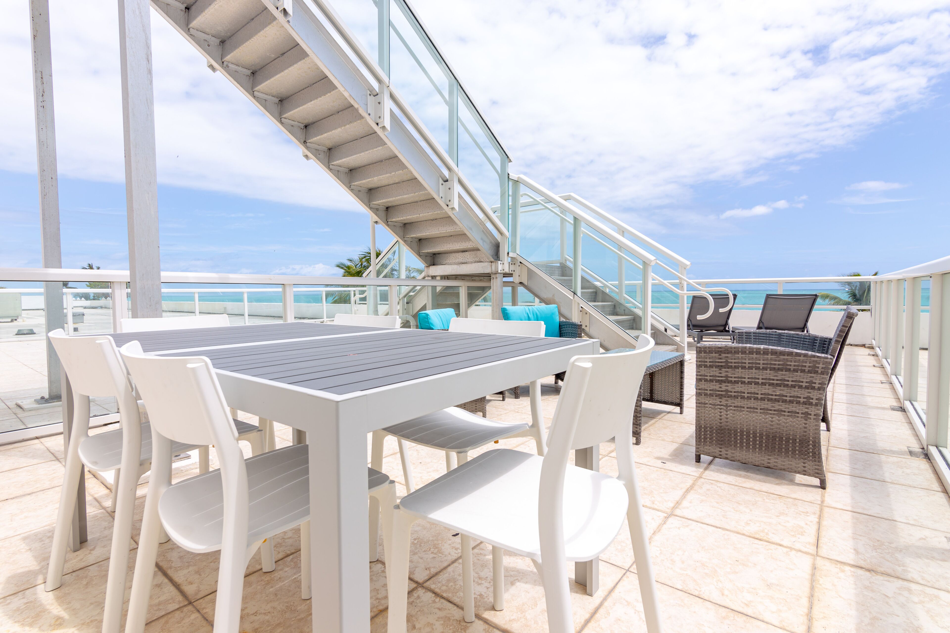 A balcony with a table and chairs, a wicker sofa, and a staircase leading to a terrace.