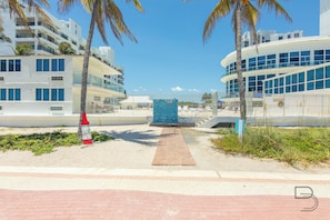 A pathway leading to a building with a blue mosaic wall, surrounded by palm trees and modern architecture.