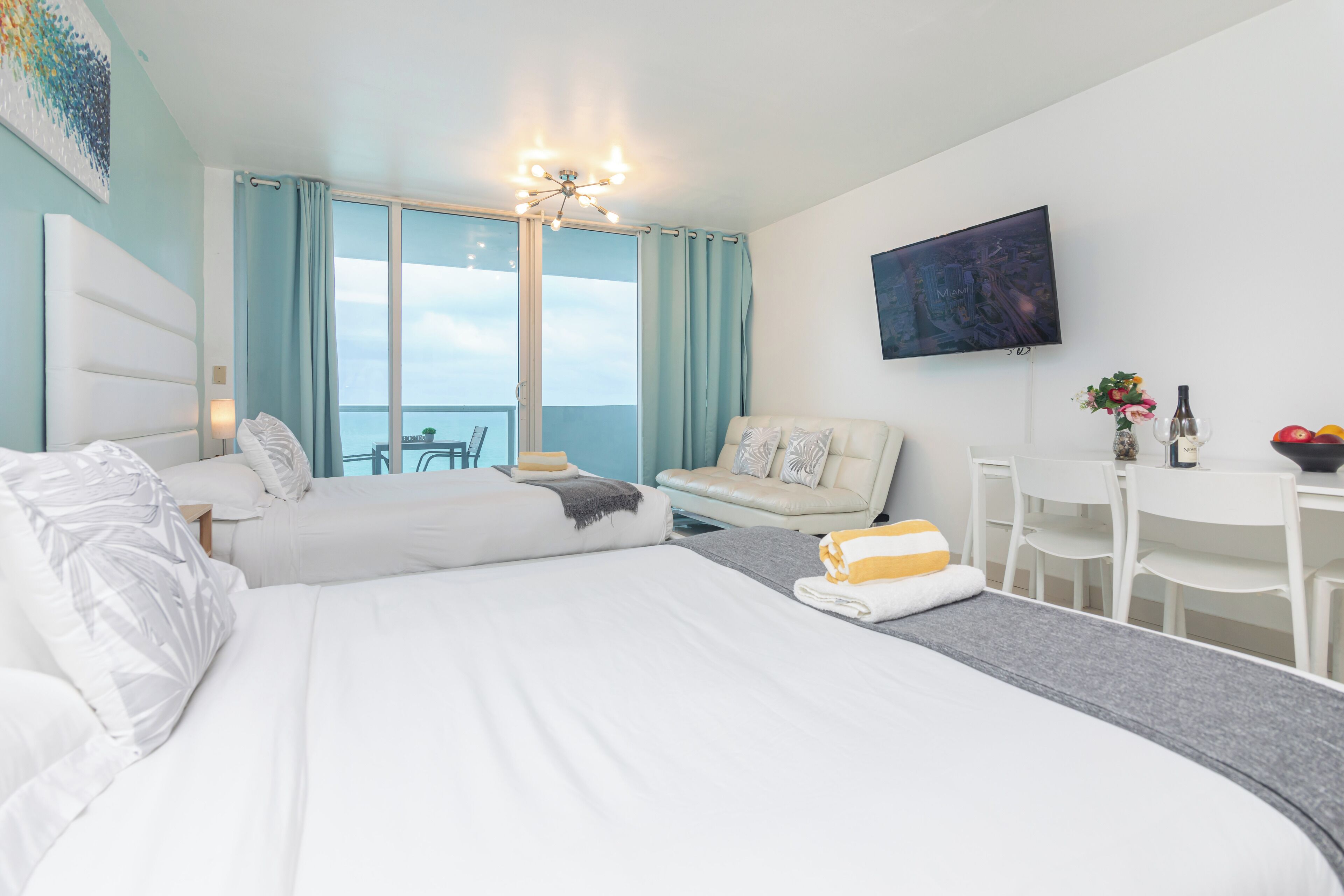 A hotel room with two beds, a TV, a dining area, and a balcony with a view.