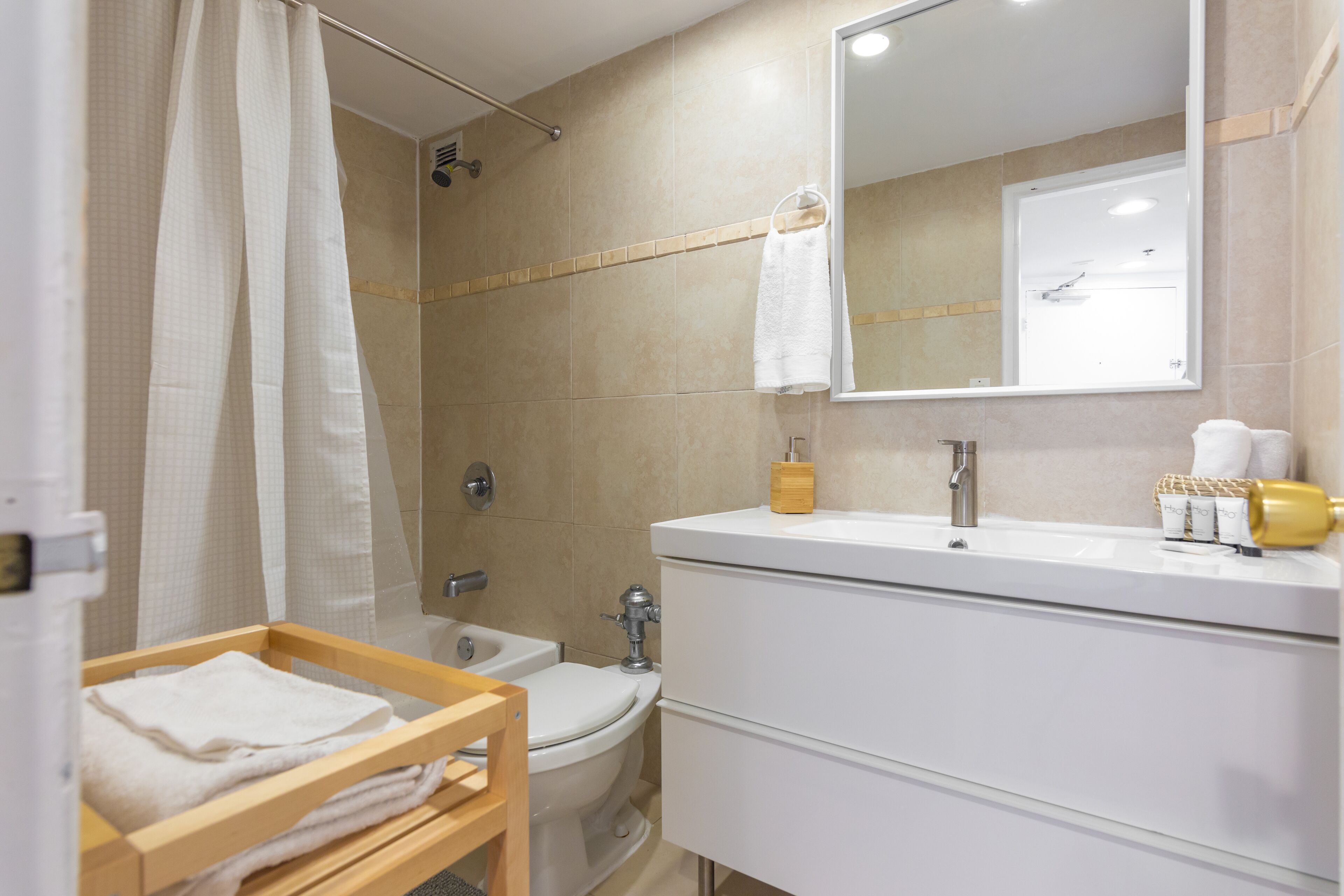 A bathroom with a shower, toilet, sink, and a wooden towel rack.
