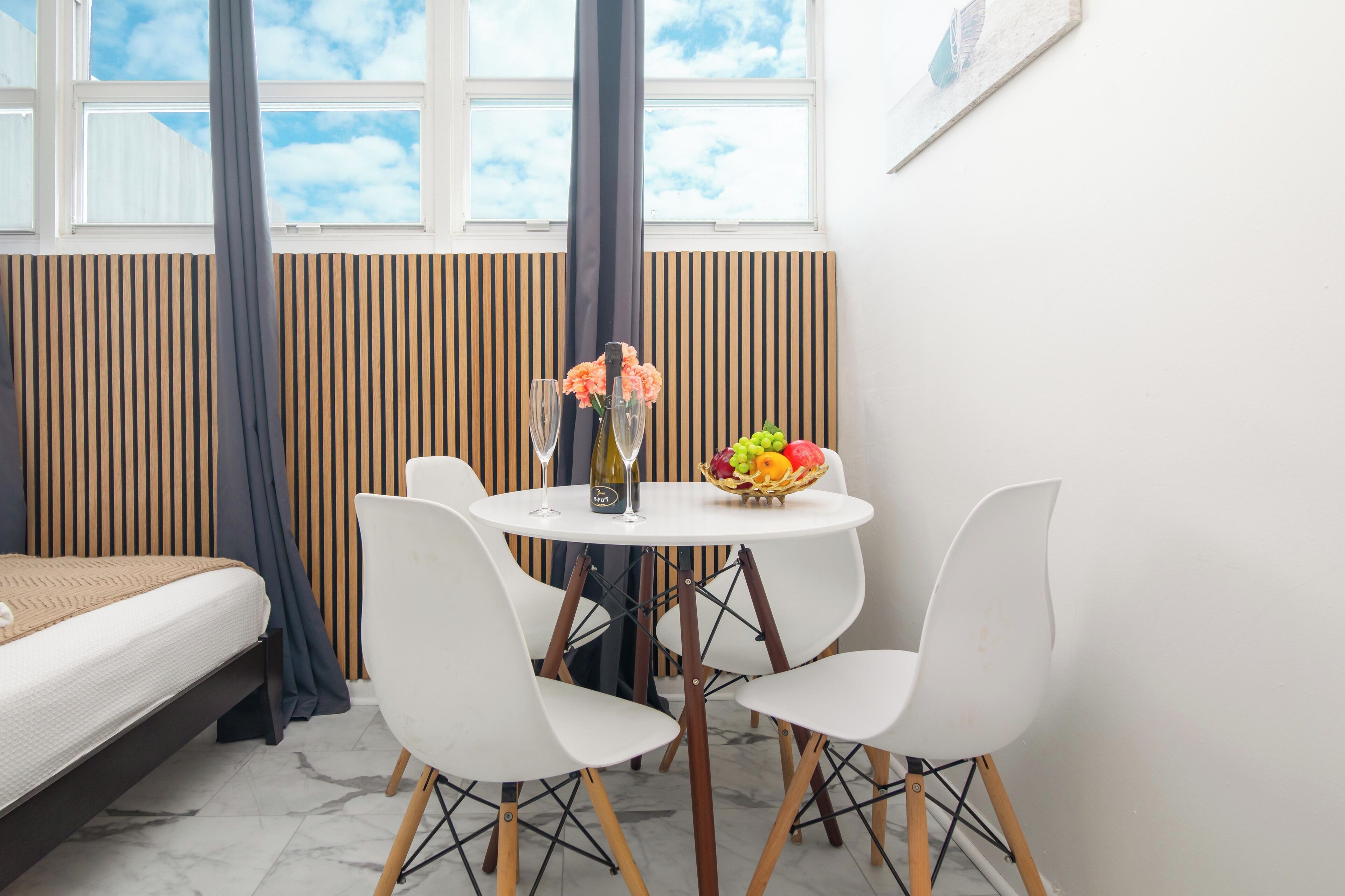 Una habitación moderna con una cama, una mesa de comedor con sillas, un frutero y un florero con flores.
