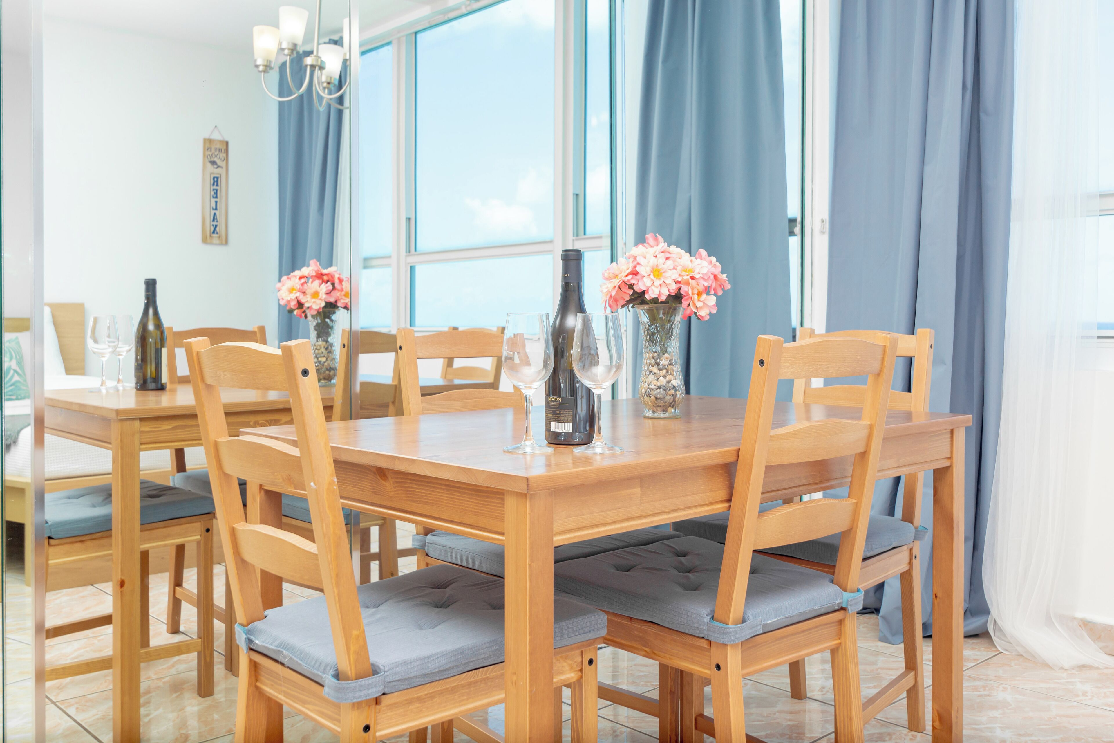 A wooden dining table with six chairs, each with a cushioned seat. There are two vases with flowers on the table.