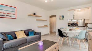 Una sala de estar moderna con un sofá gris, una mesa de centro y un comedor con una mesa y sillas blancas.