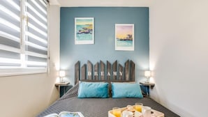 Un dormitorio con cama, dos obras de arte en la pared, cabecera de madera, dos mesitas de noche con lámparas y una bandeja con alimentos para el desayuno.