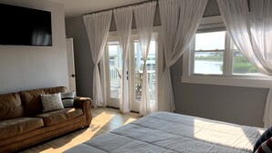 A bedroom with a large bed, a brown leather sofa, and a TV mounted on the wall.