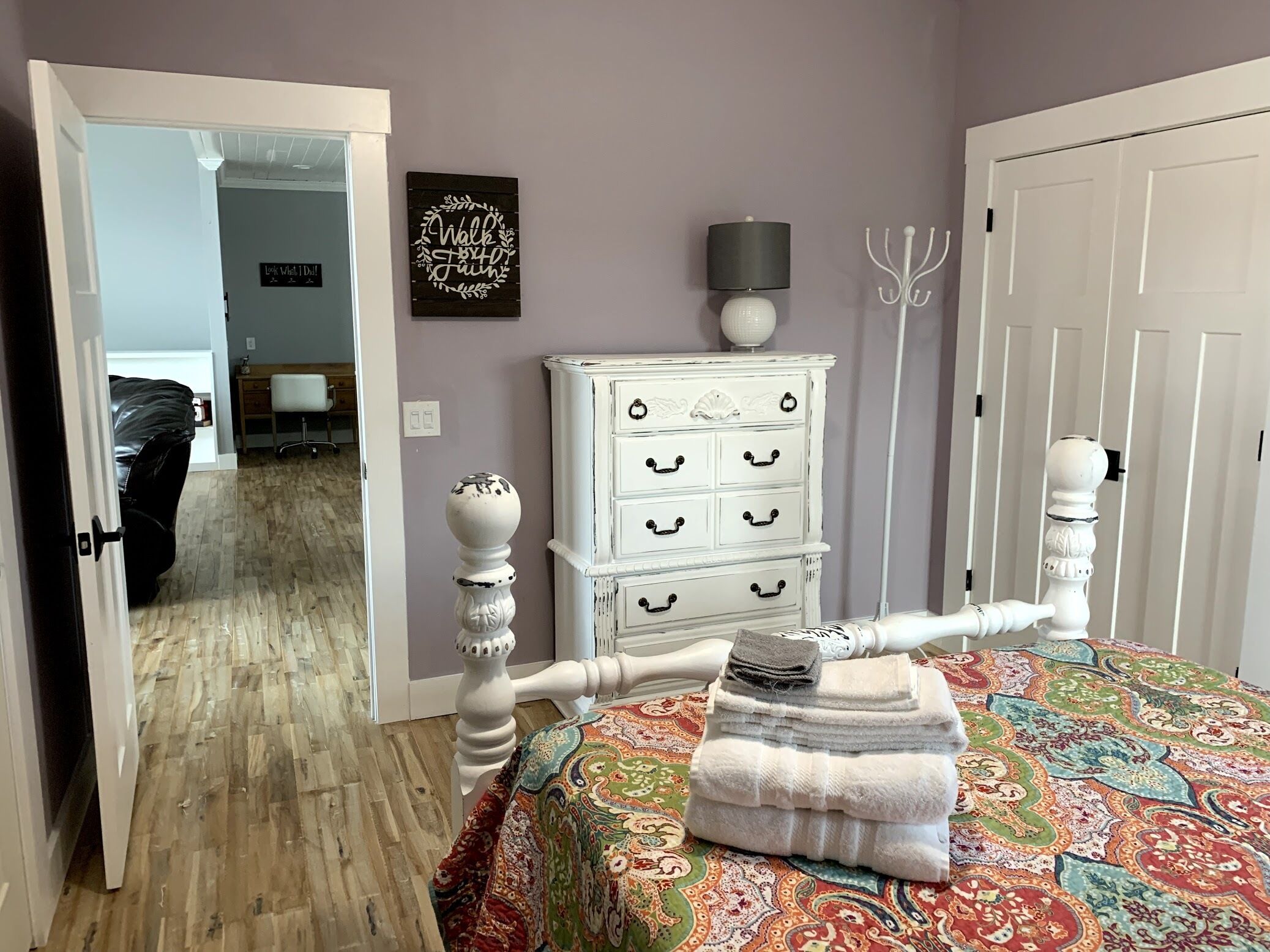 Une chambre à coucher comprenant un lit, une commode, un élément décoratif mural et une porte donnant sur une autre pièce.