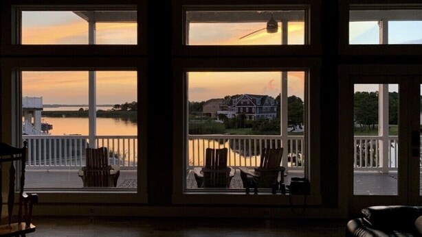 A room with large windows overlooking a body of water and a distant house.
