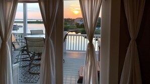 A view from a balcony with a table and chairs, overlooking a body of water and a sunset.