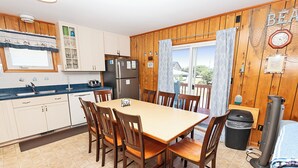 Une cuisine avec des meubles de rangement en bois, un réfrigérateur, une table à manger avec des chaises et une fenêtre avec des rideaux.