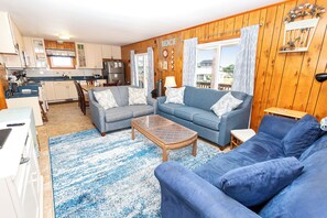 A living room with a blue sofa, a wooden coffee table, and a kitchen in the background.