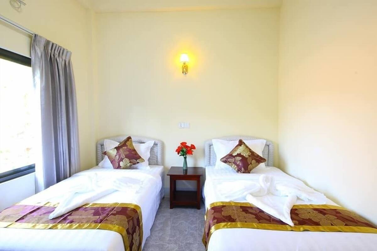 Een hotelkamer met twee enkele bedden, een klein nachtkastje met een bloevas en een wandlamp.