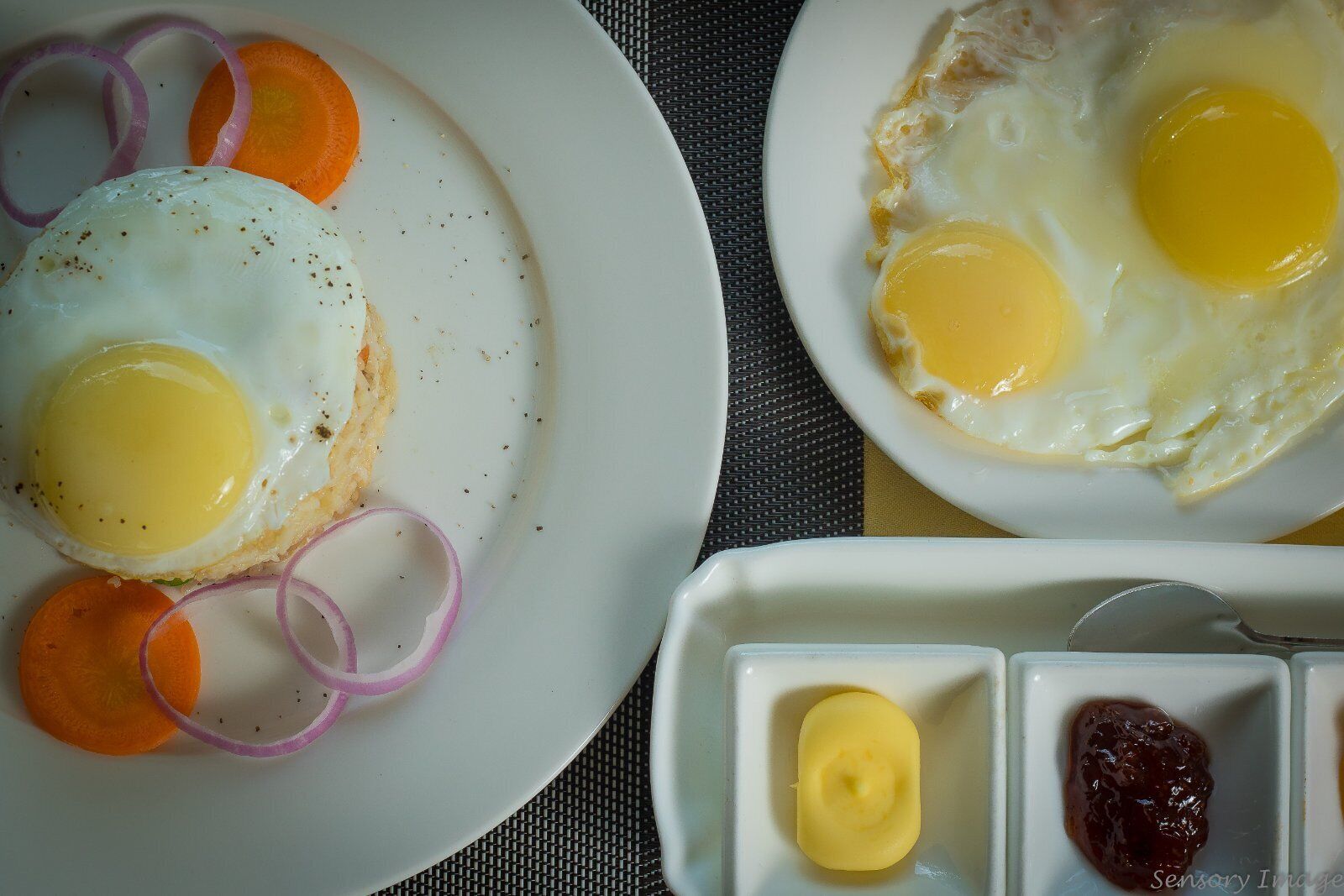 Two plates with fried eggs and sliced vegetables.