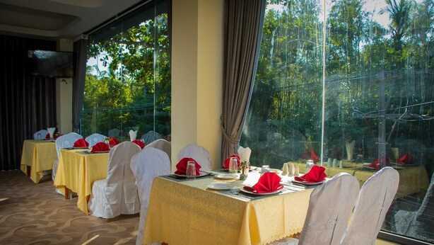 A dining area with tables set for a meal, large windows, and a view of trees.