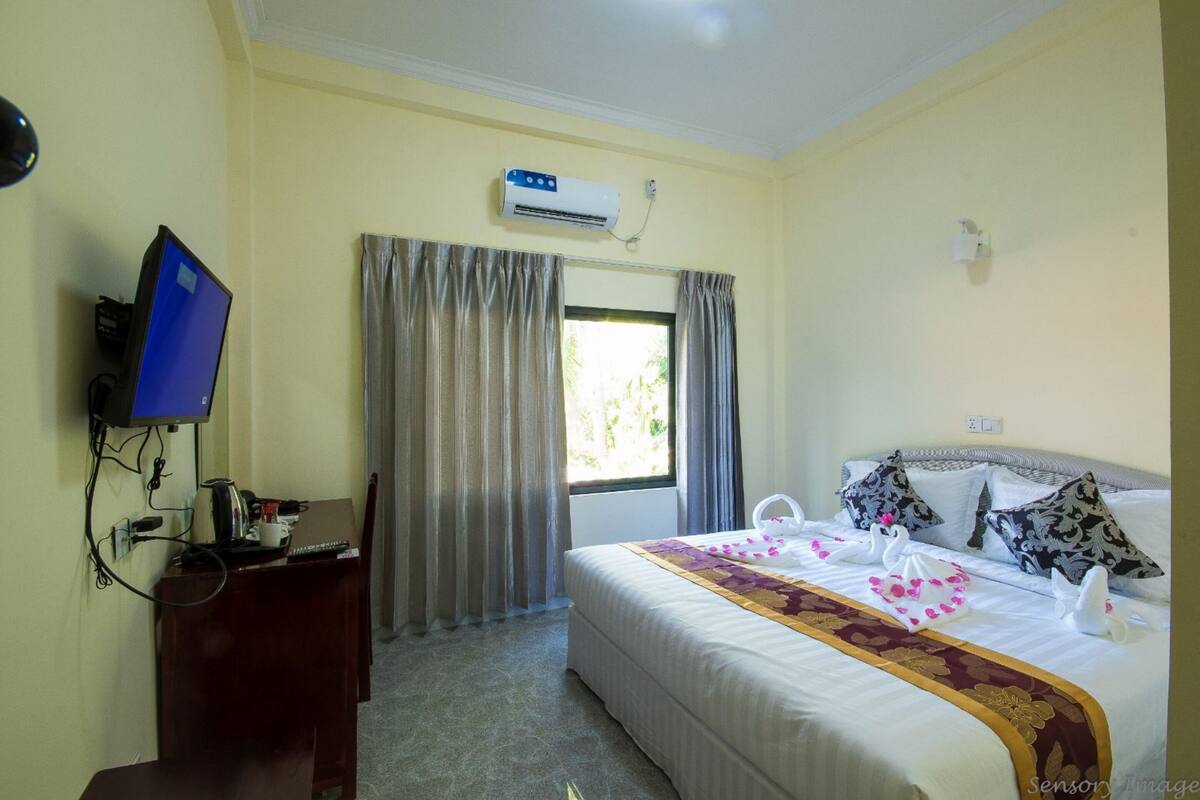 Een hotelkamer met een bed, een bureau met een computer, een airconditioner en een raam met gordijnen.