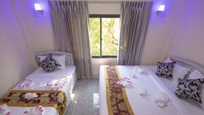 A hotel room with two beds, each with a floral bedspread and pillows, a window with curtains, and wall-mounted lights.