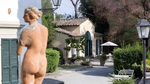 A statue of a woman in a courtyard with a building in the background, a bench, and a lamp post.