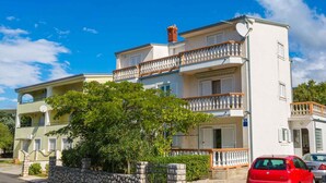 Un edificio de dos pisos con balcones, una pared de piedra y un coche rojo estacionado.
