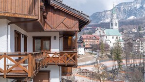 A wooden chalet with a balcony, a church with a green roof, and a mountainous backdrop. - Cortina Lodge Stunning View R&R (Cortina d´Ampezzo)