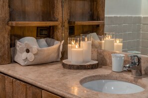 Un baño con tocador de madera, lavamanos blanco y velas sobre un posavasos de madera.