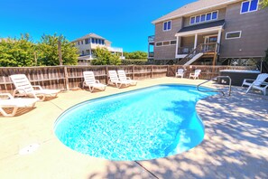 A swimming pool with lounge chairs, a wooden fence, and a two-story building in the background.