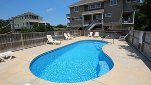 A rectangular swimming pool with a wooden deck, surrounded by white lounge chairs and a wooden fence. - Oceanside, Screened Porch Dining, Priv Pool, Yard, WW1042, Jolly Octopus (Corolla)