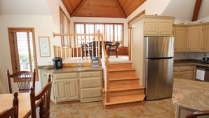 A kitchen with wooden cabinets, a stainless steel refrigerator, and a wooden staircase leading to a dining area. - Oceanside, Screened Porch Dining, Priv Pool, Yard, WW1042, Jolly Octopus (Corolla)