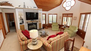 A spacious living room with a fireplace, striped sofas, and a television. - Oceanside, Screened Porch Dining, Priv Pool, Yard, WW1042, Jolly Octopus (Corolla)