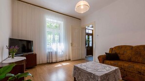 A living room with a television, a sofa, a table with a lace tablecloth, and a plant. - Holiday home mit Klimaanlage und Grill (Jadranovo)