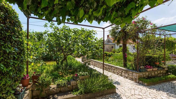 A garden with stone pathways, potted plants, and a pergola structure. - Holiday home mit Klimaanlage und Grill (Jadranovo)