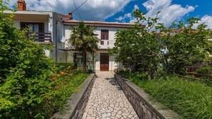 A stone pathway leading to a white building with a red-tiled roof, surrounded by lush greenery and flowering plants. - Holiday home mit Klimaanlage und Grill (Jadranovo)