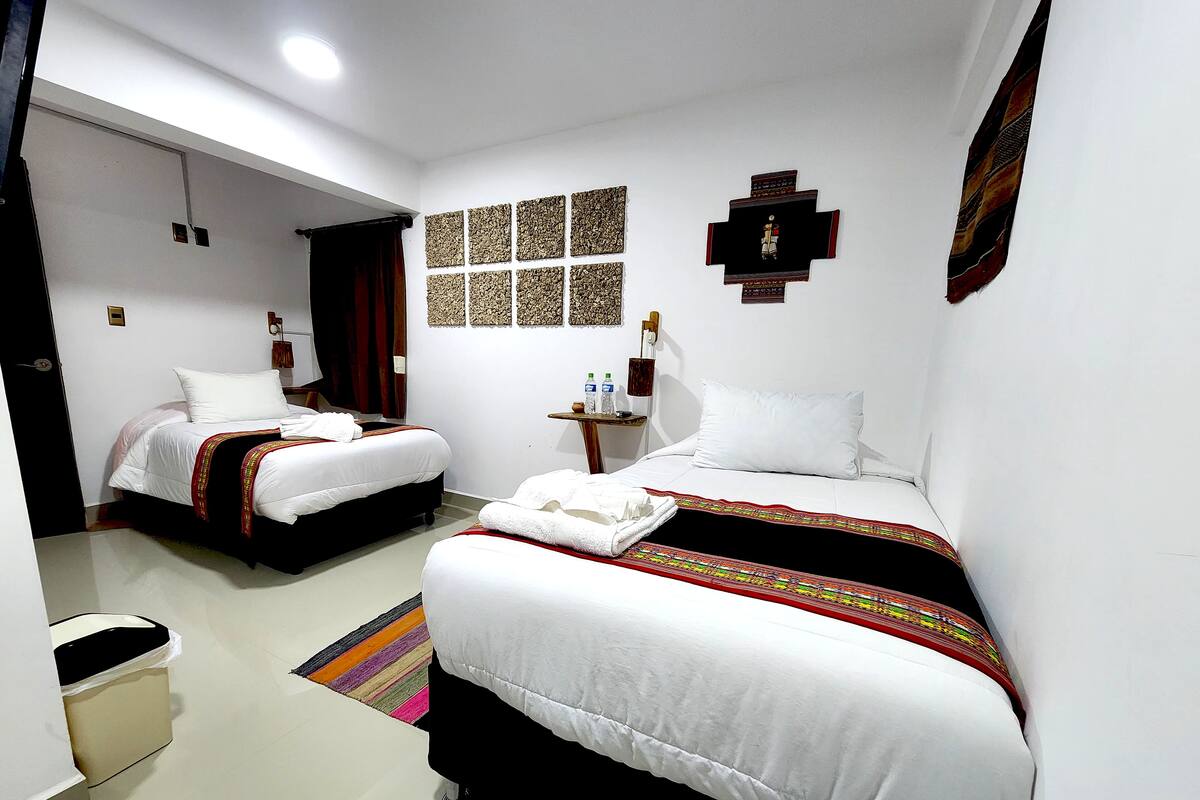 A hotel room with two beds, a small table with a lamp, and a wall with decorative panels.