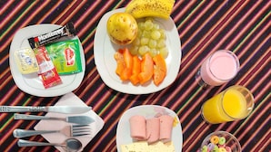 Uma mesa de café da manhã com pratos de ovos, torradas, frutas e suco sobre uma toalha listrada.