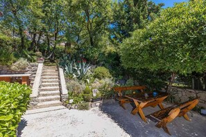 A garden with a stone staircase leading up, surrounded by lush greenery and a wooden bench area. - Holiday home 80 m from the sea (Crikvenica)