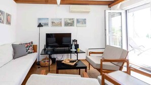 A living room with a sofa, a coffee table, and a TV. There are pictures on the wall and a window with a view. - Holiday home 80 m from the sea (Crikvenica)