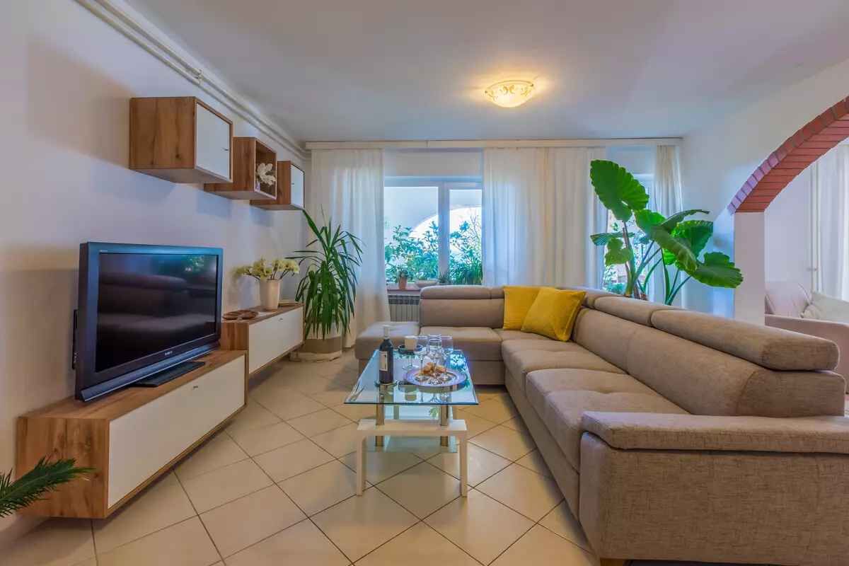 Een woonkamer met een televisie, bank, salontafel en planten.