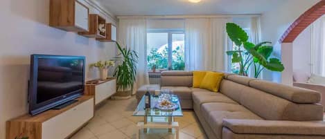 Een woonkamer met een televisie, bank, salontafel en planten.