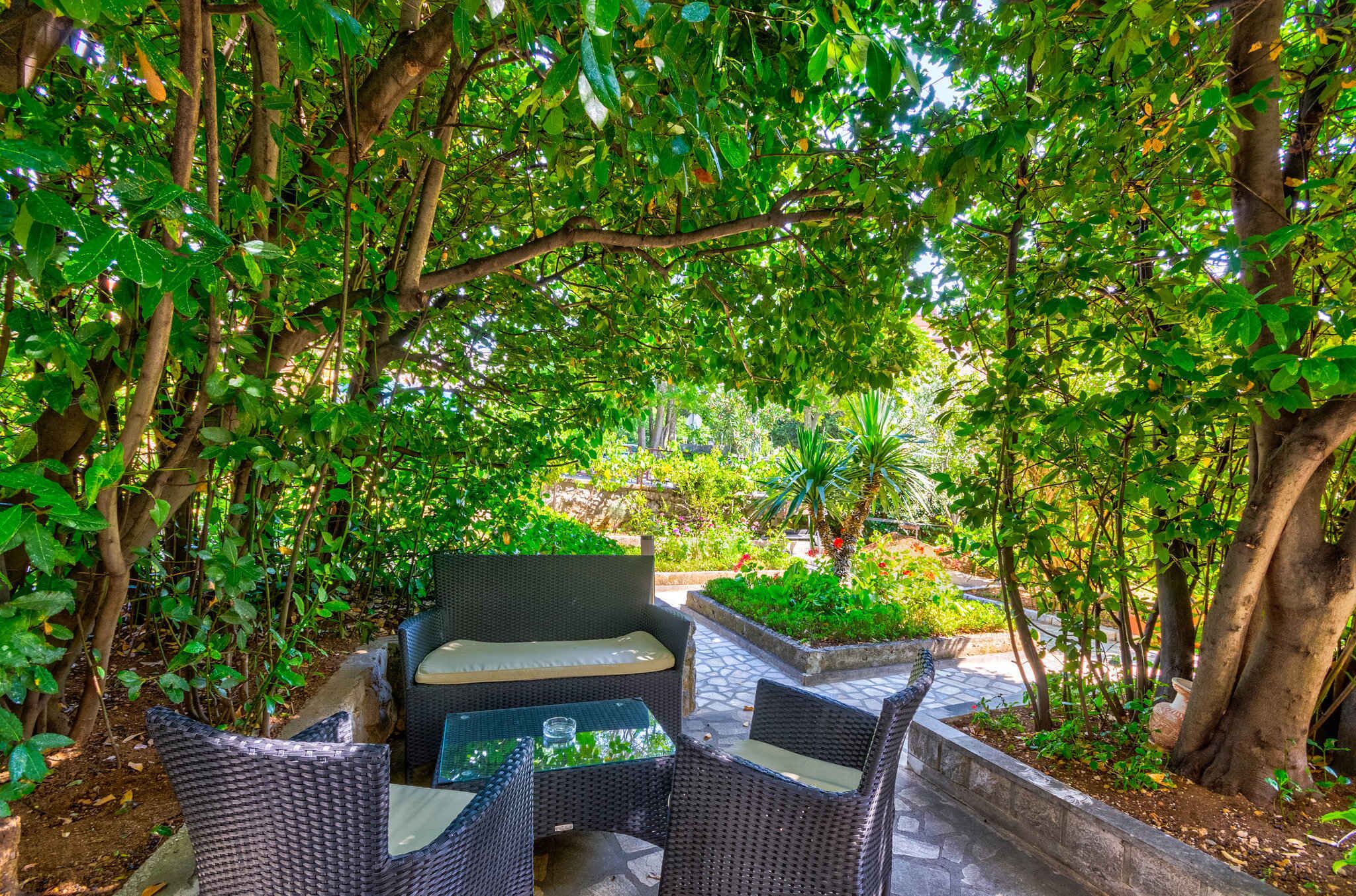 An outdoor seating area with wicker furniture and a stone pathway surrounded by lush greenery.