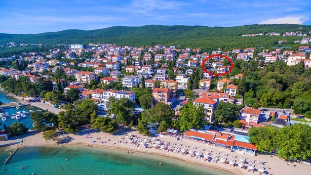 Eine Vogelperspektive auf eine Küstenstadt mit Strand, klarem türkisblauem Wasser und dicht bebauten Häusern mit roten Dächern.
