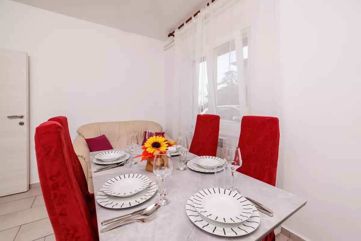 A dining table set with plates, cutlery, and glasses, surrounded by red upholstered chairs.