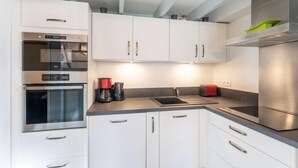 Une cuisine moderne avec des meubles blancs, des appareils en acier inoxydable et un plan de travail gris.