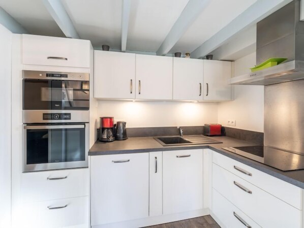 Une cuisine moderne avec des meubles blancs, des appareils en acier inoxydable et un plan de travail gris.