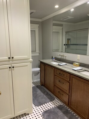 A bathroom with a white toilet, a large mirror, wooden cabinets, and a marble countertop.