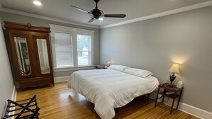 A bedroom with a large bed, wooden floor, a ceiling fan, a nightstand with a lamp, and a mirror. - Park Avenue Loft overlooking Parkerson Avenue (Crowley)