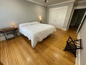 A bedroom with a wooden floor, a bed with white bedding, a nightstand with a lamp, and a wardrobe.