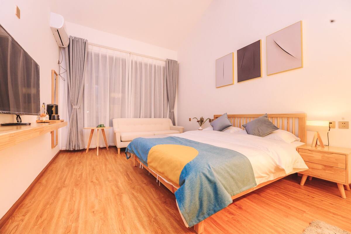 A modern bedroom with a large bed, a bedside table, a nightstand, a TV, and a window with curtains.
