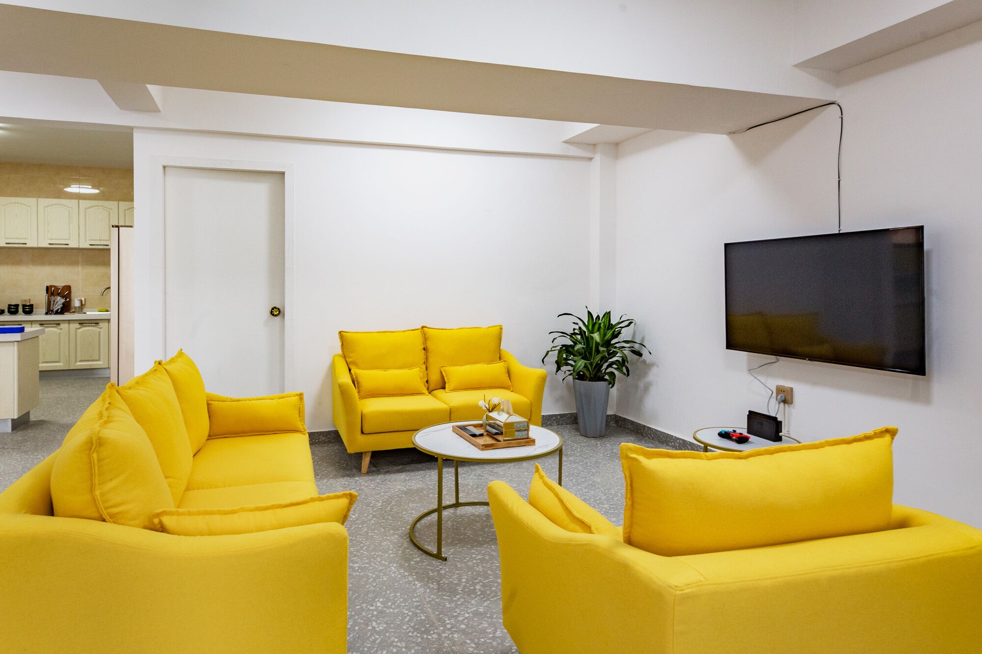 A living room with yellow sofas, a coffee table, a potted plant, and a TV mounted on the wall.