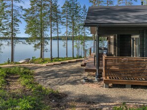 Une cabane dotée d’une terrasse donnant sur un lac, entourée d’arbres.