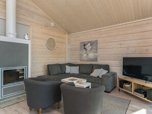 A modern living room with a sofa, two armchairs, a coffee table, a fireplace, a television, and a wall-mounted clock.